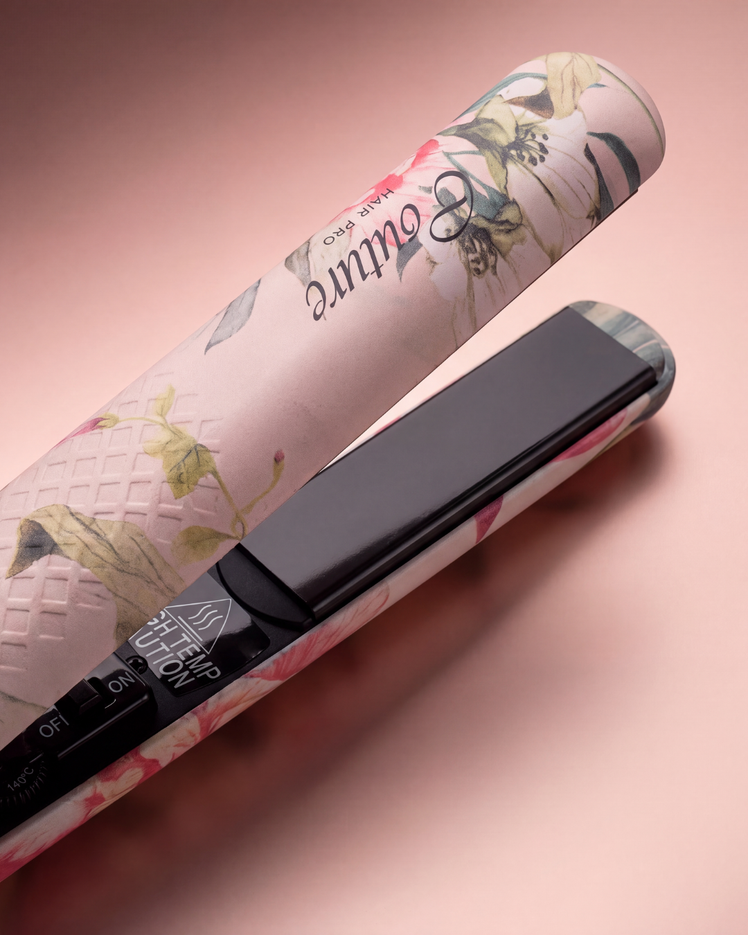 A flat hair straightener with a pink floral patterned body and a black control panel, shown diagonally on a soft pink background. The brand name 'e couture' is visible on the handle.
