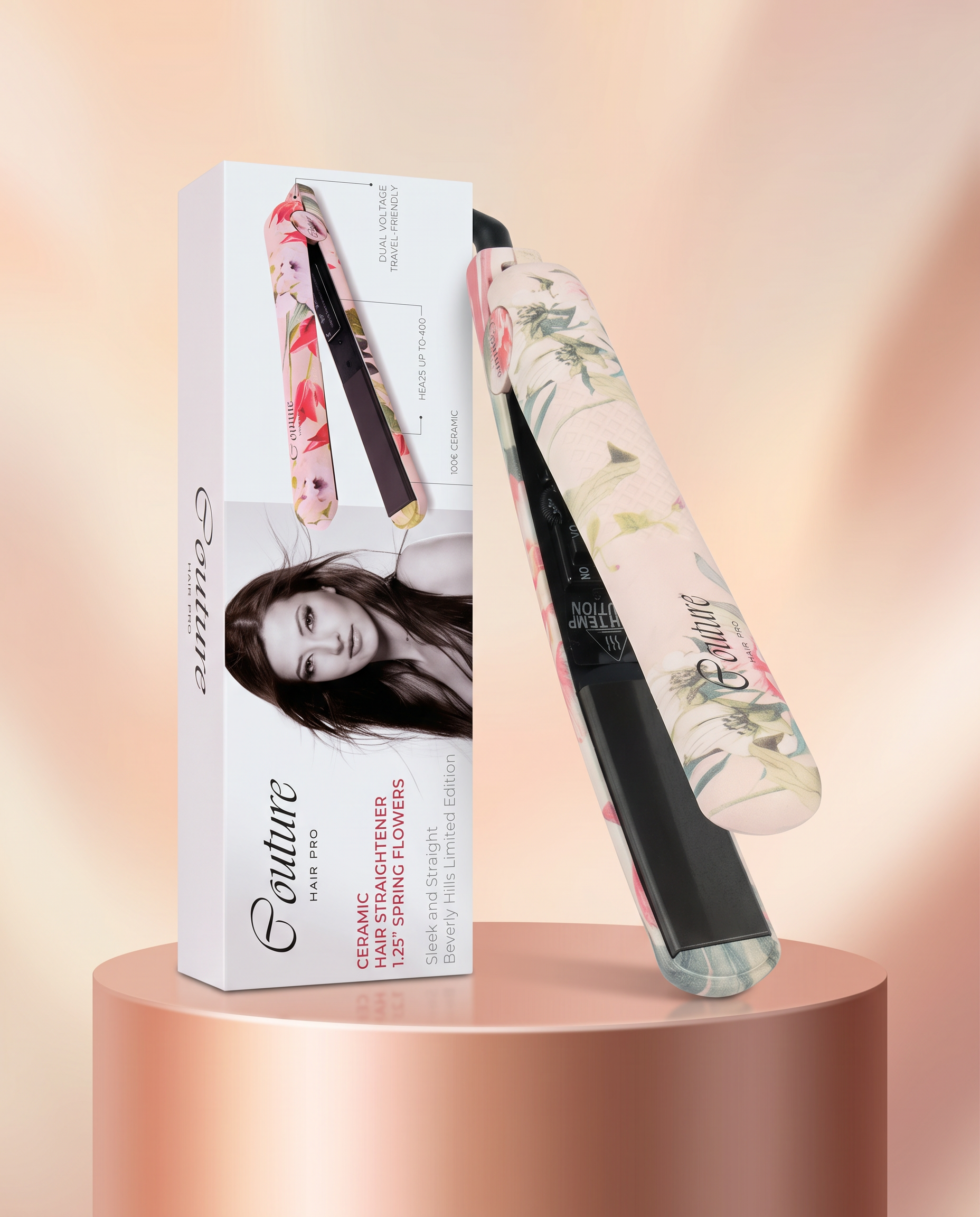 A Couture Paris hair straightener with a floral patterned handle, shown next to its white retail box on a metallic rose-gold pedestal against a soft peach background.