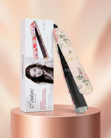A Couture Paris hair straightener with a floral patterned handle, shown next to its white retail box on a metallic rose-gold pedestal against a soft peach background.